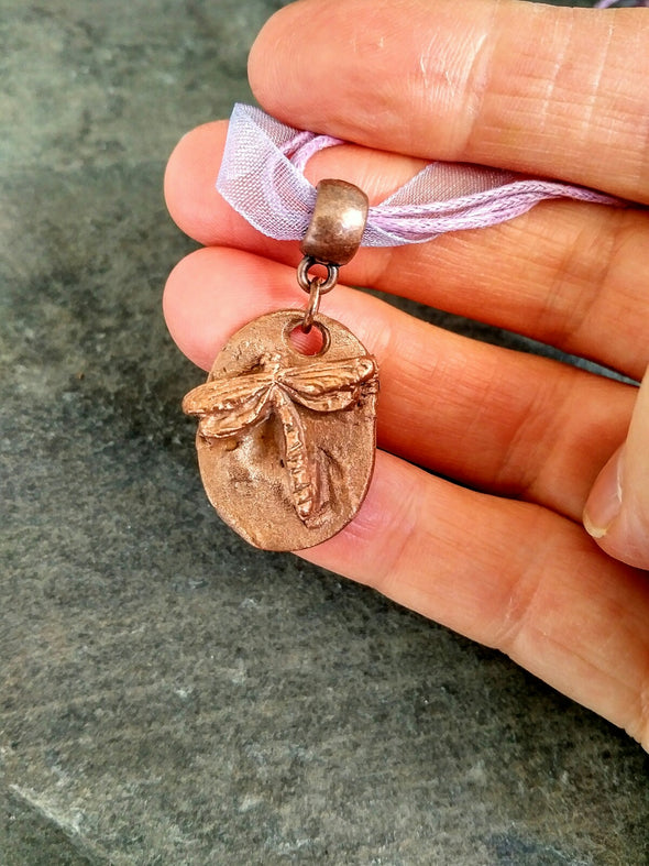Copper dragonfly necklace held to show size
